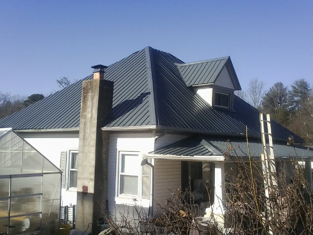Dark blue standing seam metal roof on a white farmhouse with dormer in Sweetser