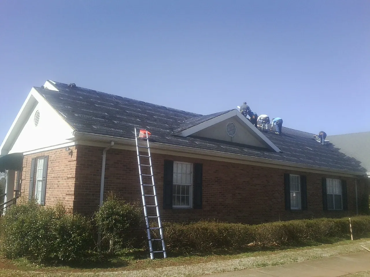 Crew tearing shingles off a brick ranch roof with a ladder set — Metal Roof Repair work by our crew in Sweetser