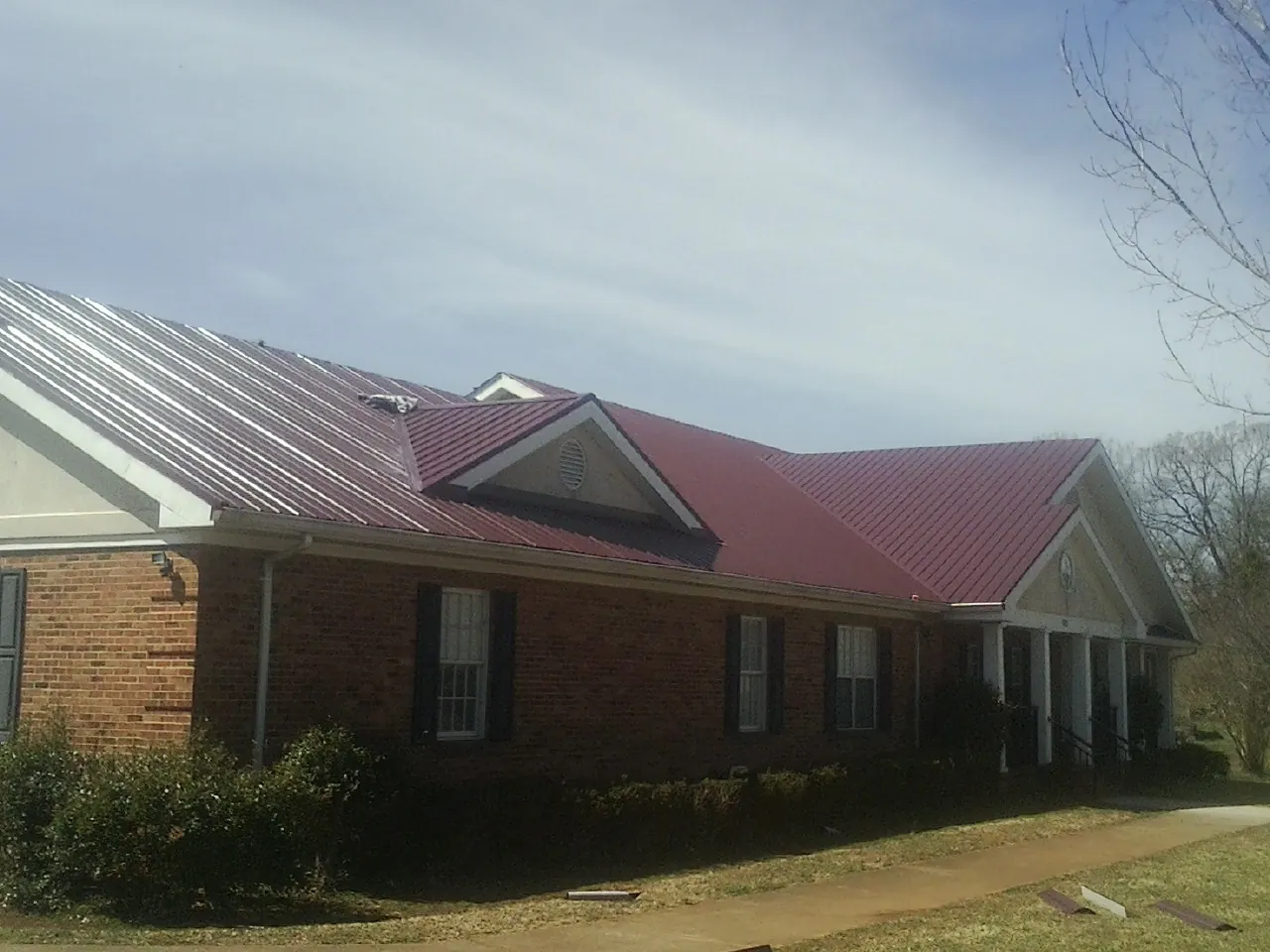 Red metal roof with gabled entries on a long brick building, from a Hail Damage Roof Repair job in Sweetser