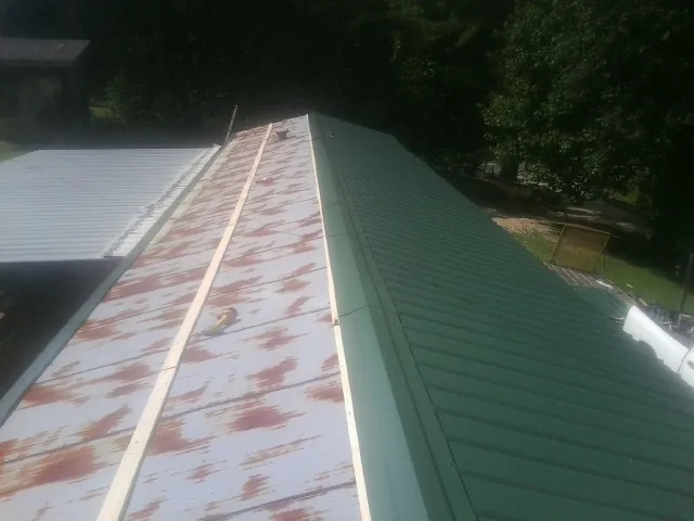 Old rusted panels beside newly installed green metal roofing — Wind Damage Roof Repair by Roofing Brothers in Sweetser