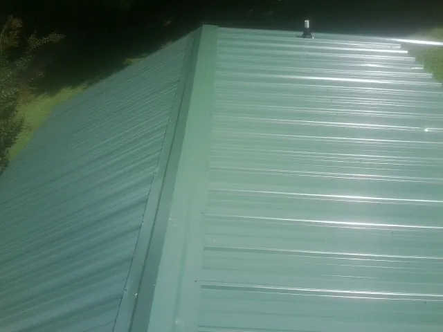 New green metal panels meeting at the ridge of a roof — Flat Roof Repair work by our crew in Sweetser