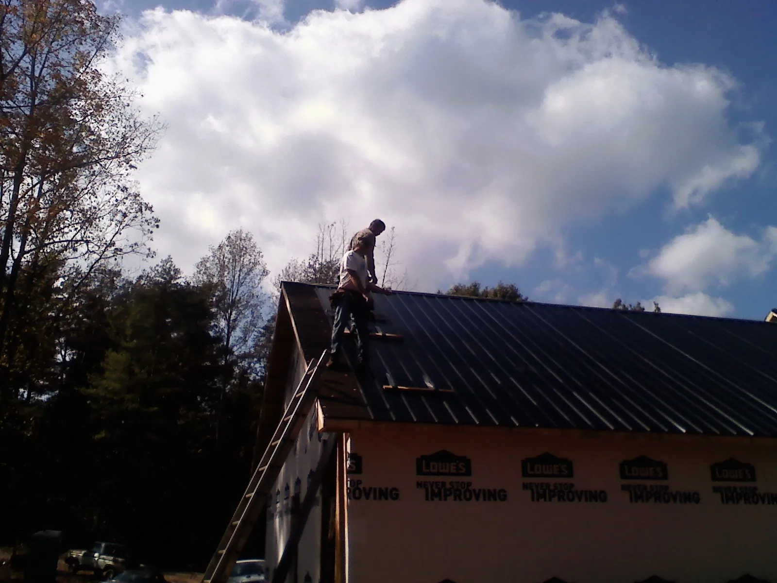 Roofer fastening dark metal panels high against a cloudy sky, from a Roof Inspection job in Sweetser