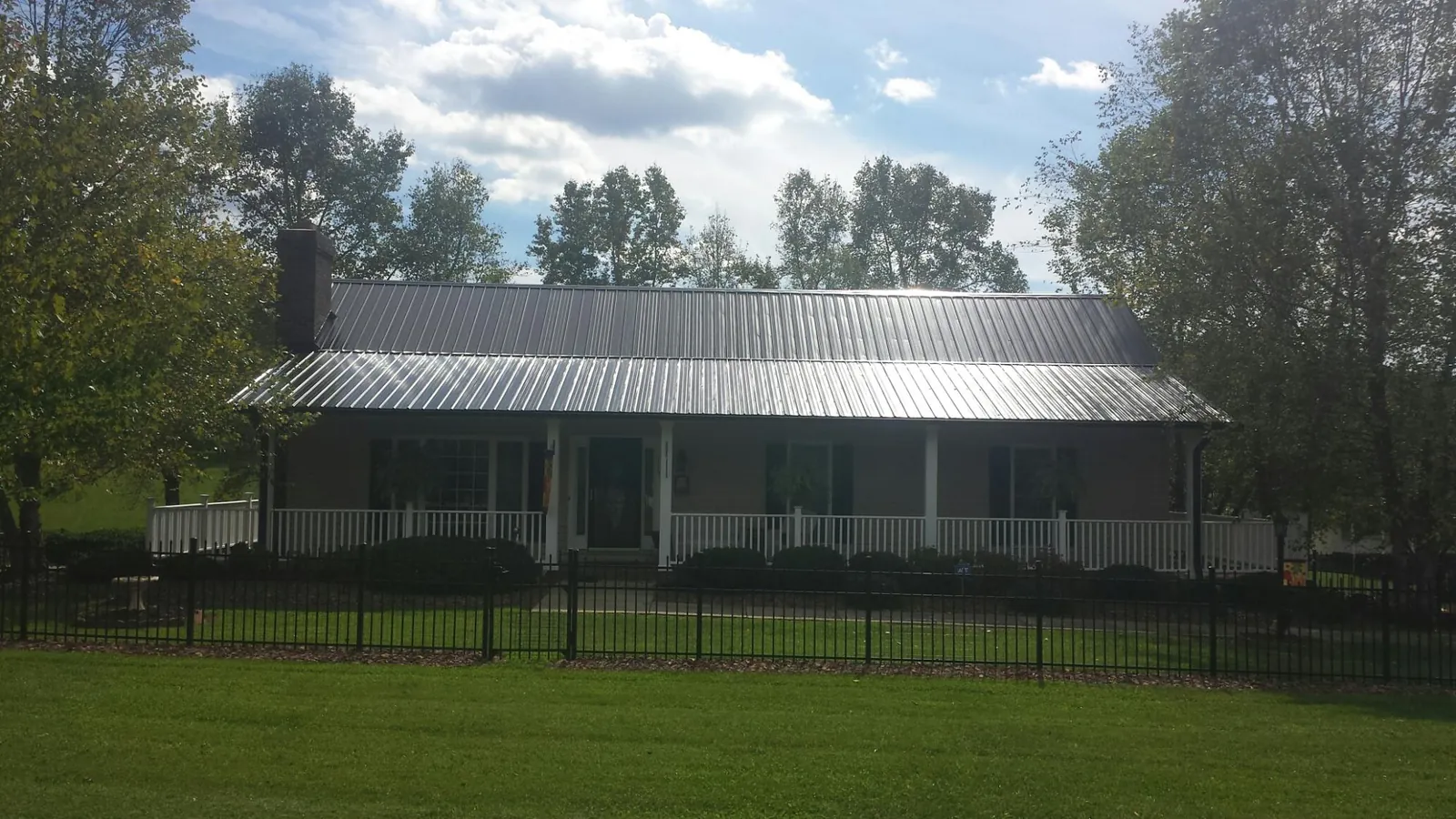 Gray metal roof on a brick ranch with a full width front porch — Gutter Guard Installation work by our crew in Sweetser
