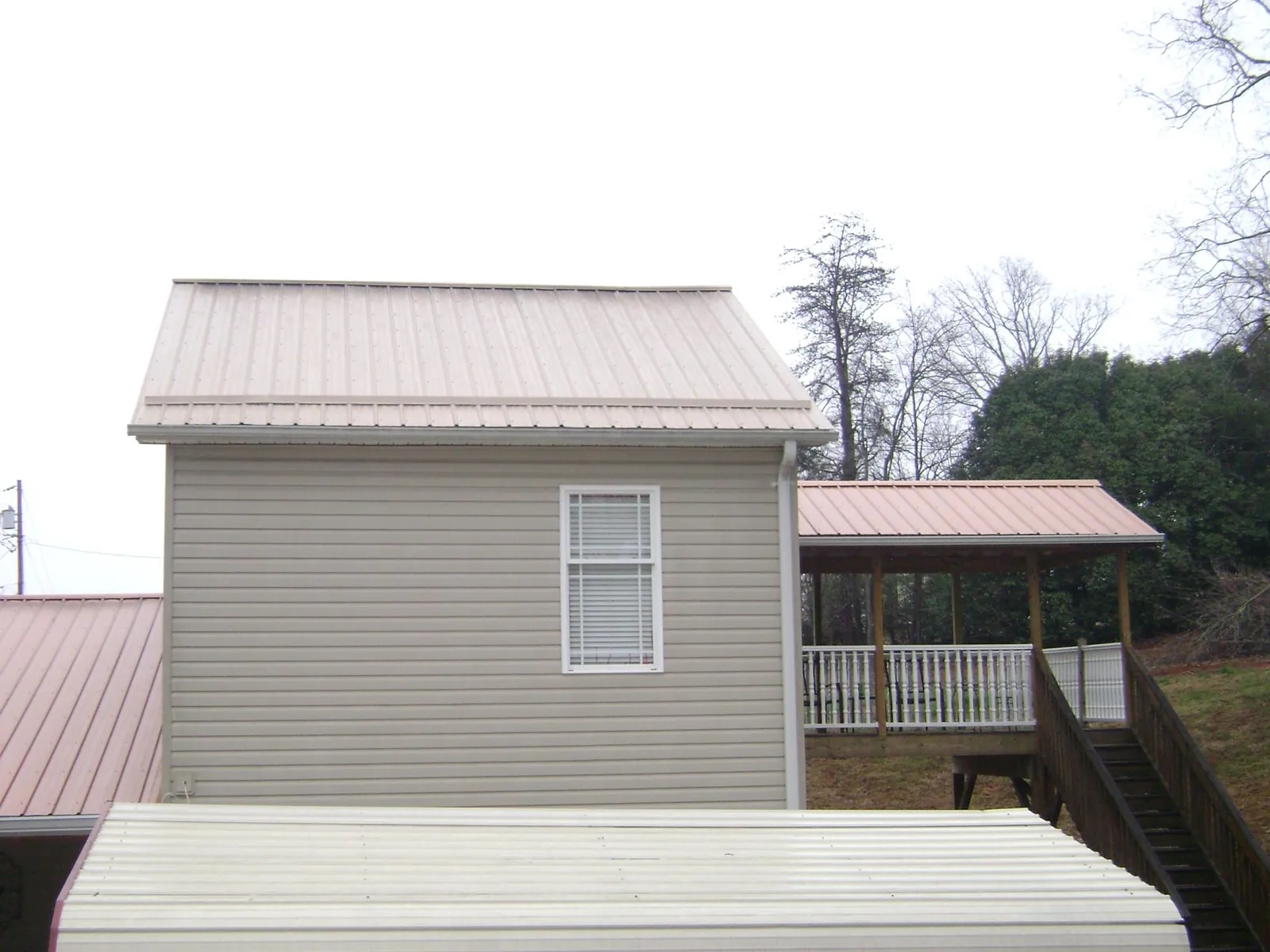 Tan metal roofs on a two story addition and attached porch, from a Roof Replacement job in Sweetser